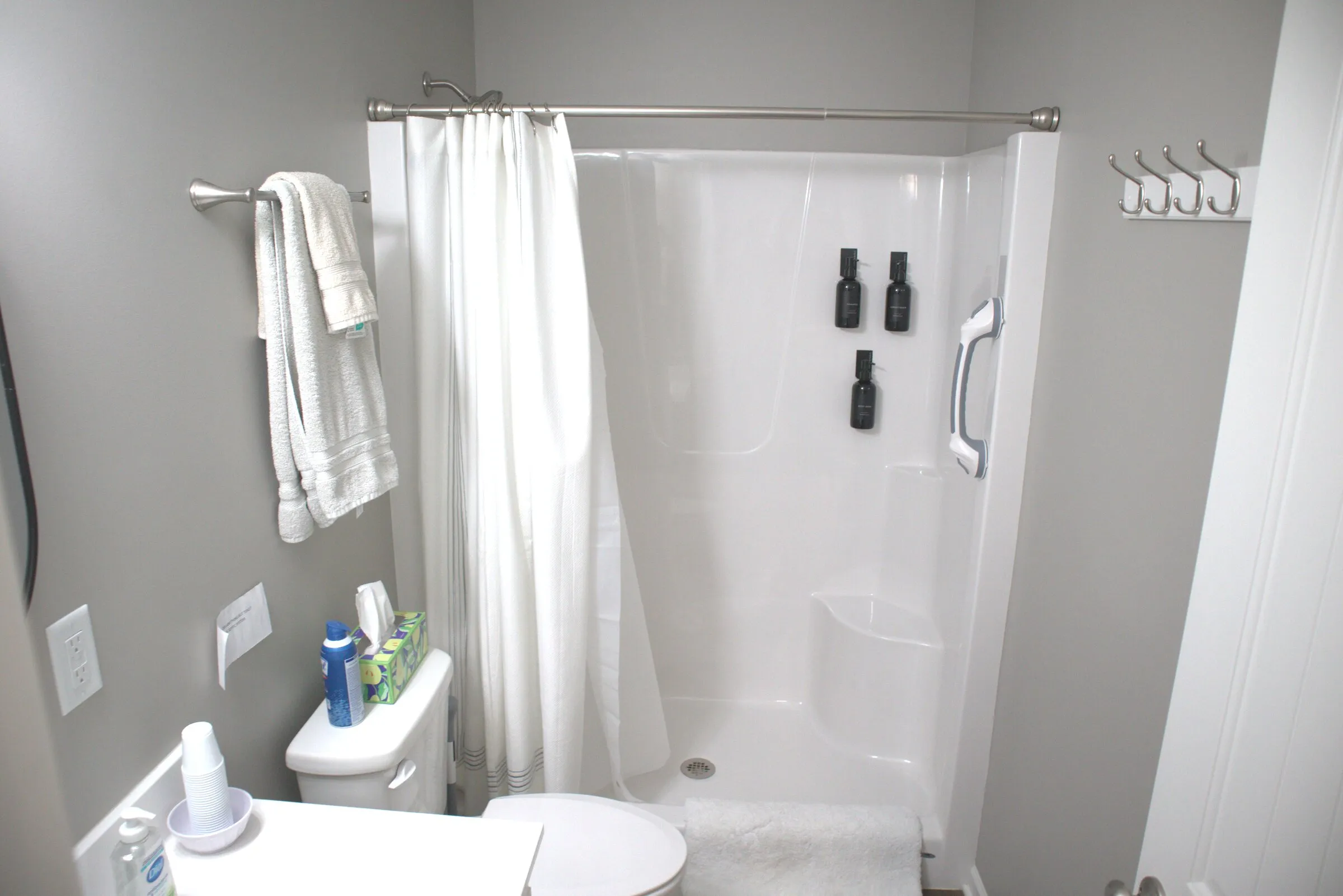 Walk-in shower with mounted dispensers, fresh towels, and hooks for personal items
