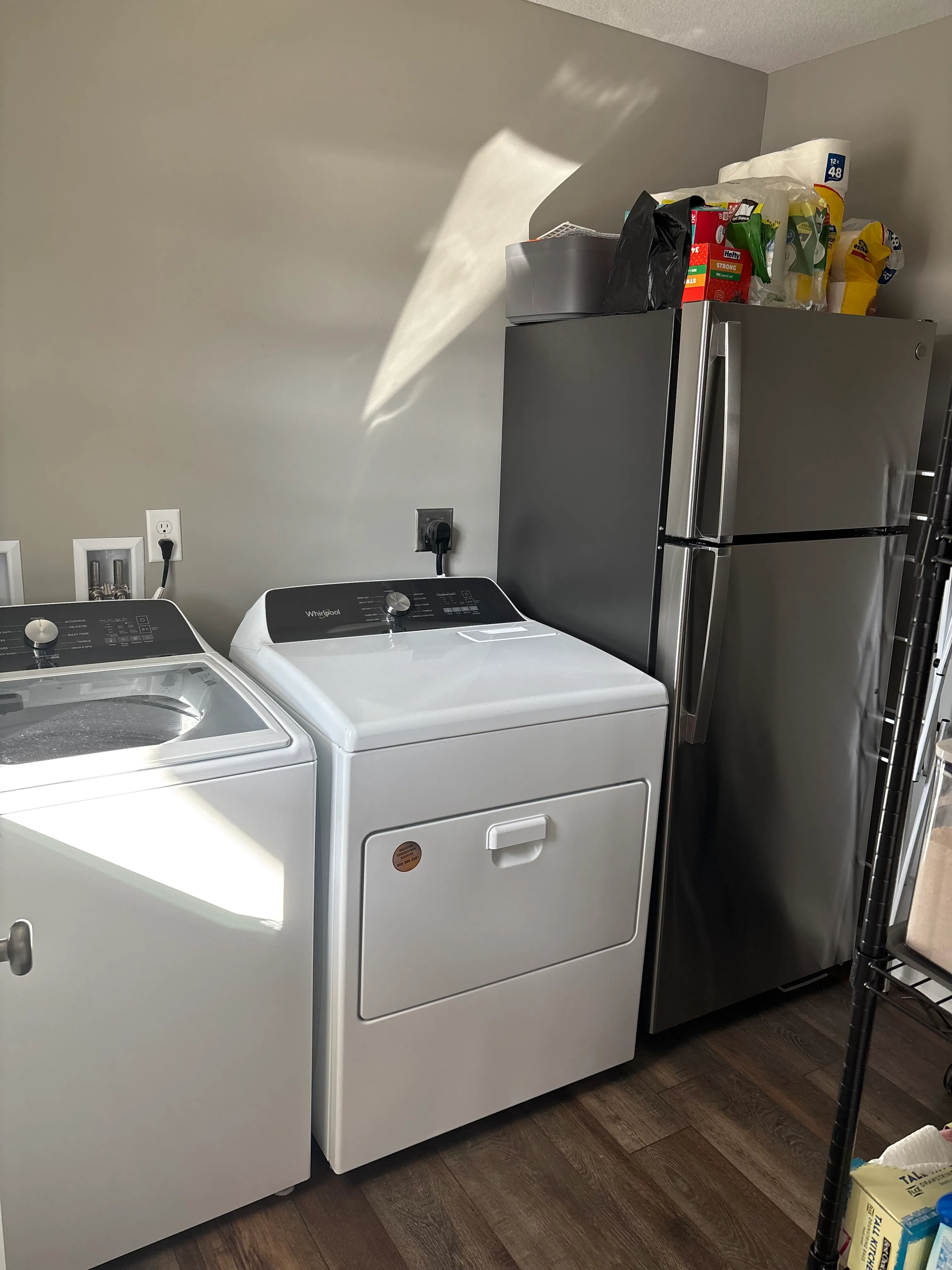Laundry room with full-size washer, dryer, and stainless steel refrigerator with storage shelving